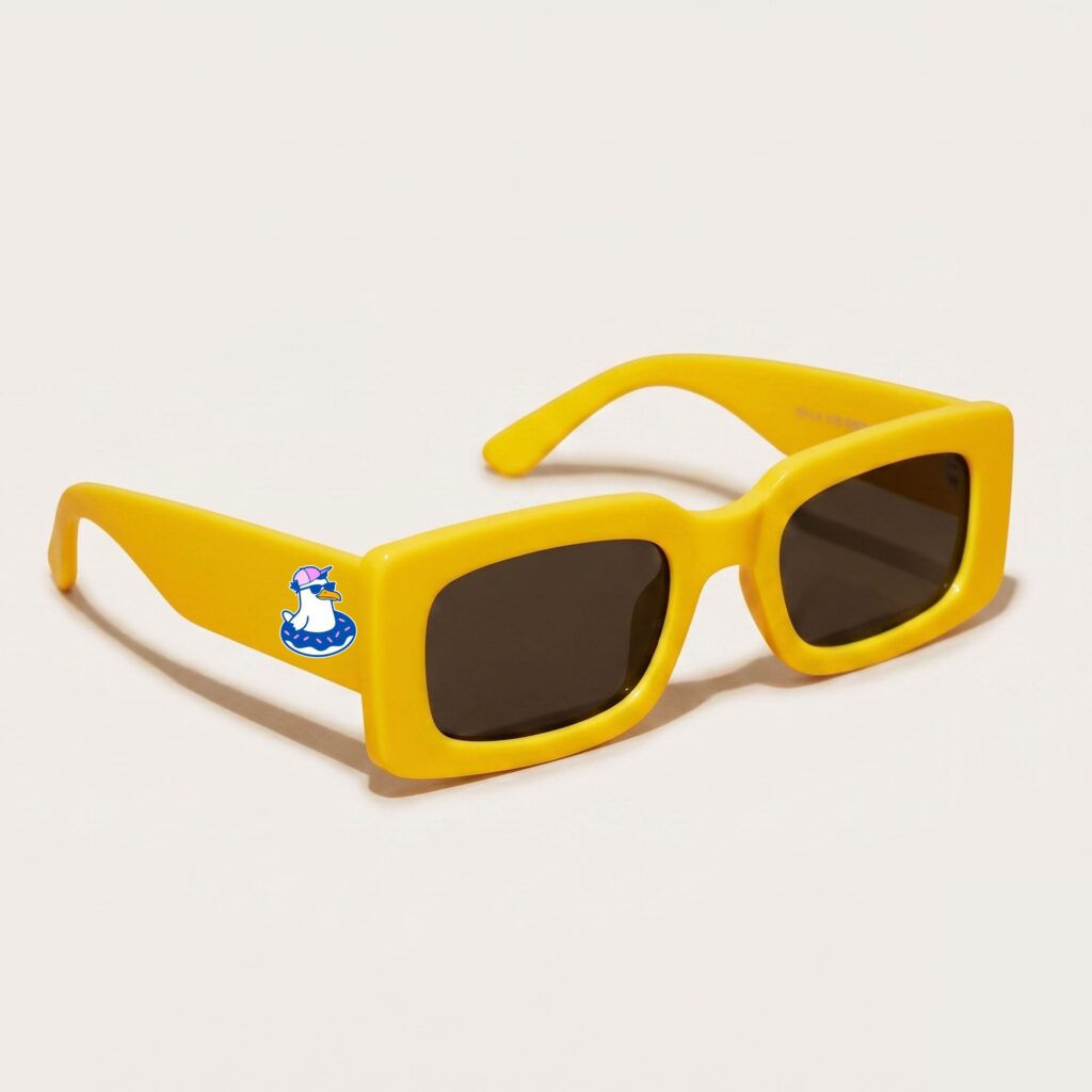 Lunettes de soleil femme tendance avec monture en plastique jaune soleil et forme rectangle, verres gris foncé, posées sur fond clair minimaliste, logo Chouchou Beignet sur la branche, accessoire plage de la collection été Marseille.