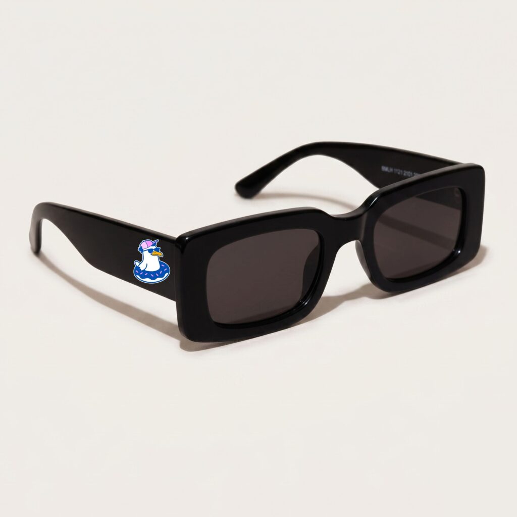 Lunettes de soleil femme tendance avec monture en plastique noir profond et forme rectangle, verres gris foncé, posées sur fond clair minimaliste, logo Chouchou Beignet sur la branche, accessoire plage de la collection été Marseille.