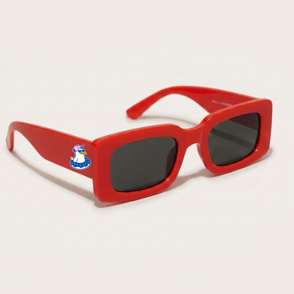 Lunettes de soleil femme tendance avec monture en plastique rouge intense et forme rectangle, verres gris foncé, posées sur fond clair minimaliste, logo Chouchou Beignet sur la branche, accessoire plage de la collection été Marseille.