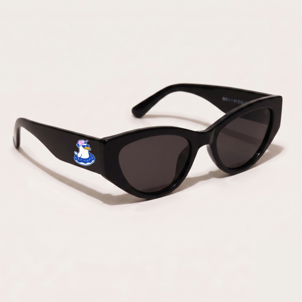 Lunettes de soleil femme tendance avec monture en plastique noir profond et forme cat-eye, verres gris foncé, posées sur fond clair minimaliste, logo Chouchou Beignet sur la branche, accessoire plage de la collection été Marseille.