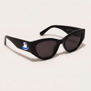 Lunettes de soleil femme tendance avec monture en plastique noir profond et forme cat-eye, verres gris foncé, posées sur fond clair minimaliste, logo Chouchou Beignet sur la branche, accessoire plage de la collection été Marseille.