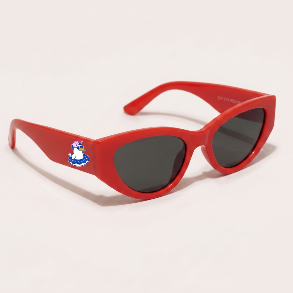 Lunettes de soleil femme tendance avec monture en plastique rouge intense et forme cat-eye, verres gris foncé, posées sur fond clair minimaliste, logo Chouchou Beignet sur la branche, accessoire plage de la collection été Marseille.