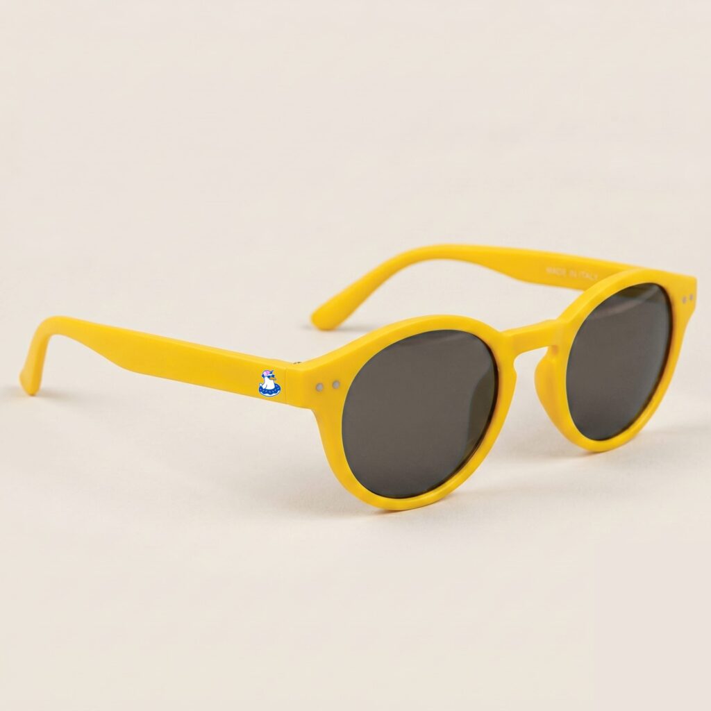 Lunettes de soleil femme tendance avec monture en plastique jaune soleil et forme pantos, verres gris teinté, posées sur fond clair minimaliste, logo Chouchou Beignet sur la branche, accessoire plage de la collection été Marseille.