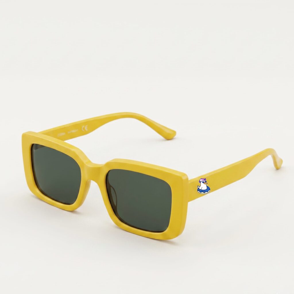 Lunettes de soleil femme tendance avec monture en plastique jaune soleil et forme carrée, verres gris foncé, posées sur fond clair minimaliste, logo Chouchou Beignet sur la branche, accessoire plage de la collection été Marseille.