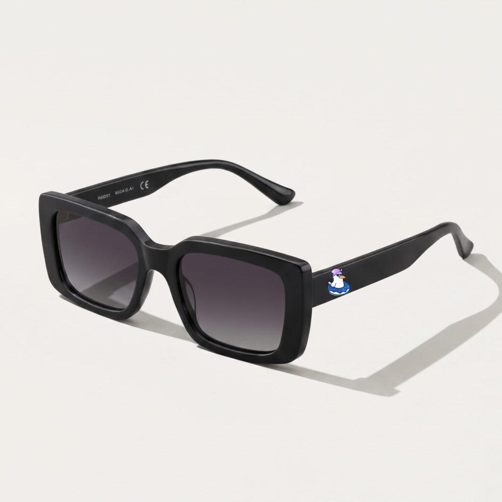 Lunettes de soleil femme tendance avec monture en plastique noir profond et forme carrée, verres gris foncé, posées sur fond clair minimaliste, logo Chouchou Beignet sur la branche, accessoire plage de la collection été Marseille.
