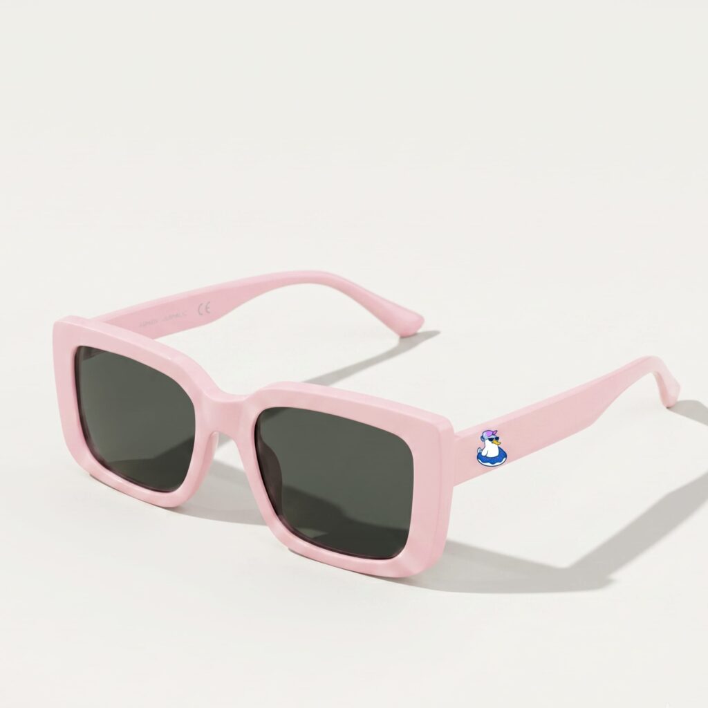 Lunettes de soleil femme tendance avec monture en plastique rose bonbon et forme carrée, verres gris foncé, posées sur fond clair minimaliste, logo Chouchou Beignet sur la branche, accessoire plage de la collection été Marseille.