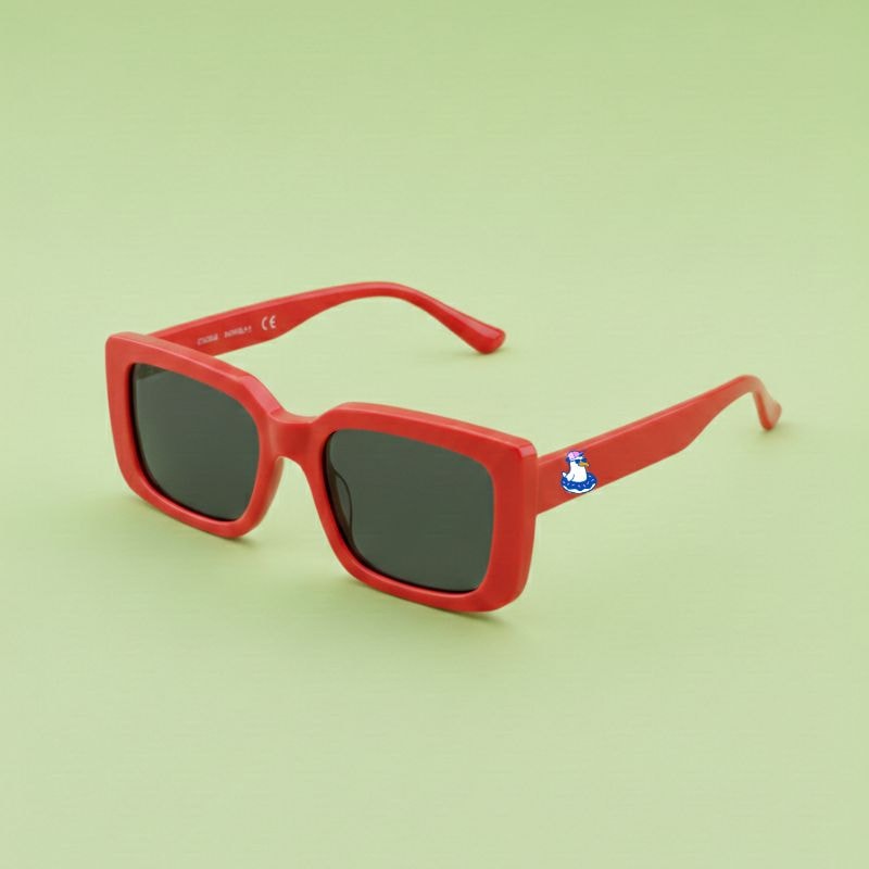 Photo lunettes de soleil modèle Droitaubut de couleur rouge intense avec le logo Chouchou Beignet sur la branche, présentées sur un fond vert éclatant, collection Chouchou Beignet Marseille.