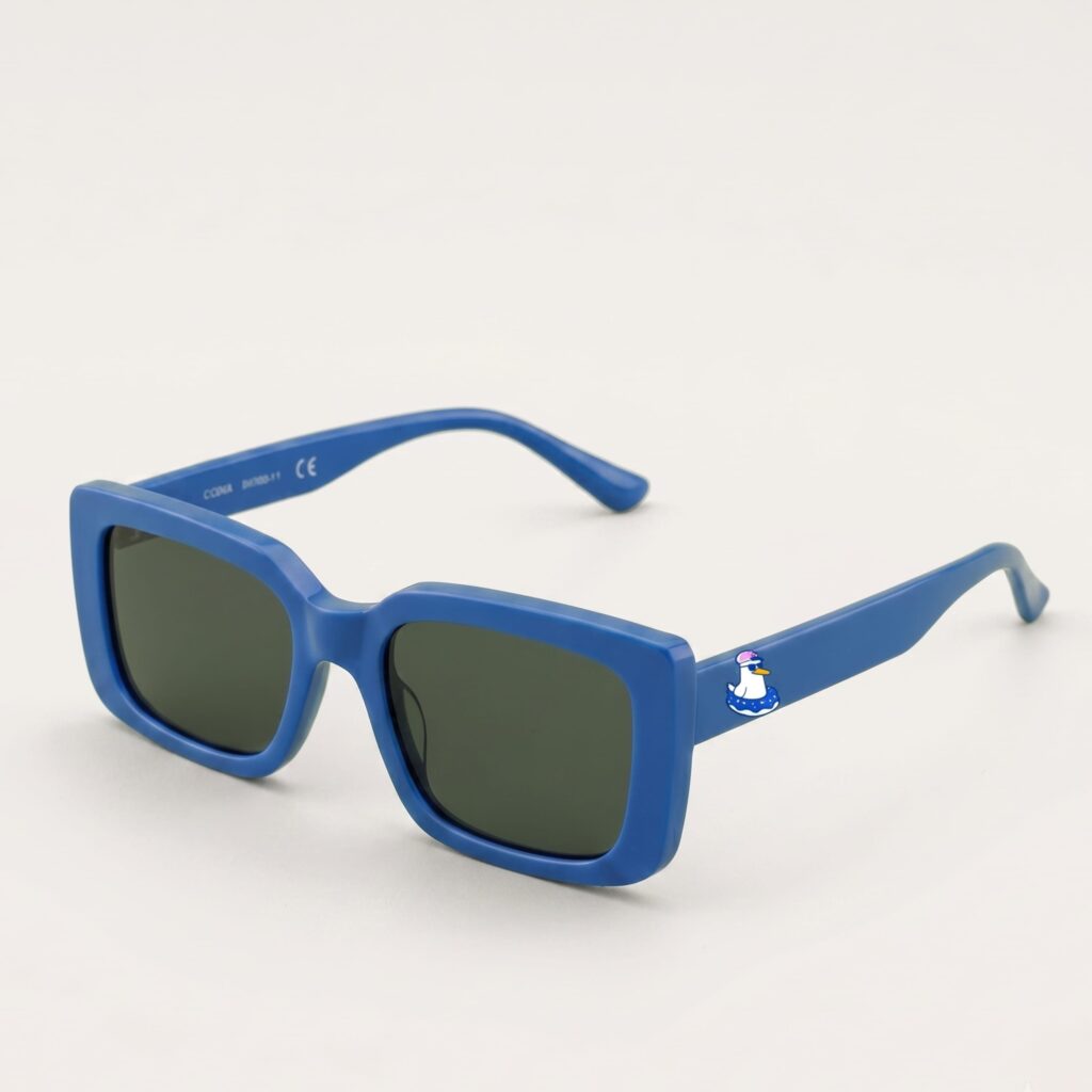 Lunettes de soleil femme tendance avec monture en plastique bleu azur et forme carrée, verres gris foncé, posées sur fond clair minimaliste, logo Chouchou Beignet sur la branche, accessoire plage de la collection été Marseille.