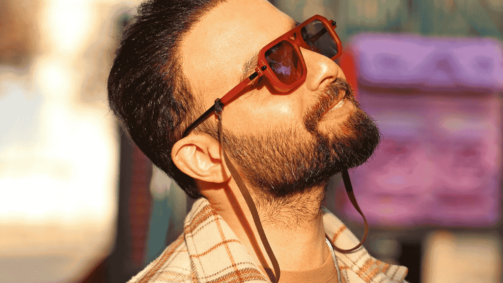 Homme barbu portant des lunettes de soleil vintage avec un cordon en cuir élégant, style mode urbaine.