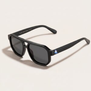 Lunettes de soleil au style aviateur revisité et tendance, se caractérisant par une monture épaisse à double pont en acétate mat de couleur noir profond. Les verres foncés affichent une teinte gris-noir qui protège un max. Présenté de trois-quarts face sur un fond blanc crème très épuré avec une élégante ombre portée sur le côté, cet accessoire plage met en avant le logo Chouchou Beignet avec son gabian en bouée sur la branche gauche, une pièce maîtresse pour la collection été Marseille.