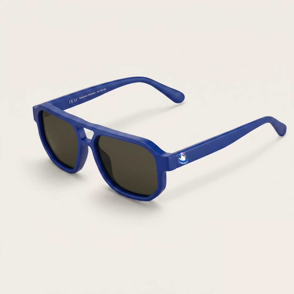 Lunettes de soleil femme tendance avec monture en métal bleu azur et forme aviateur, verres gris foncé, posées sur fond clair minimaliste, logo Chouchou Beignet sur la branche, accessoire plage de la collection été Marseille.
