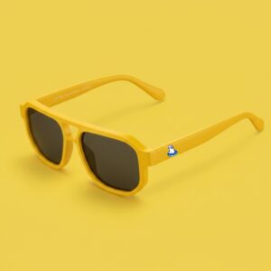 Photo lunettes de soleil modèle Mistrale de couleur jaune soleil avec le logo Chouchou Beignet sur la branche, présentées sur un fond bleu azur éclatant, collection Chouchou Beignet Marseille.