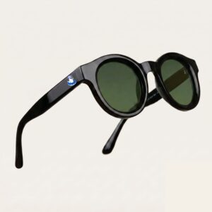 Lunettes de soleil femme tendance avec monture en plastique noir profond et forme ronde, verres gris foncé, posées sur fond clair minimaliste, logo Chouchou Beignet sur la branche, accessoire plage de la collection été Marseille.