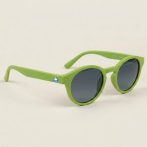 Lunettes de soleil femme au style Pantos tendance, se distinguant par une monture arrondie en acétate mat de couleur vert pomme. Les verres foncés affichent une teinte gris sombre hautement protectrice. Présenté de trois-quarts face sur un fond beige sable très doux et épuré, cet accessoire plage incontournable met en avant le logo Chouchou Beignet avec son gabian en bouée sur la branche droite, une pièce maîtresse pour la collection été Marseille.